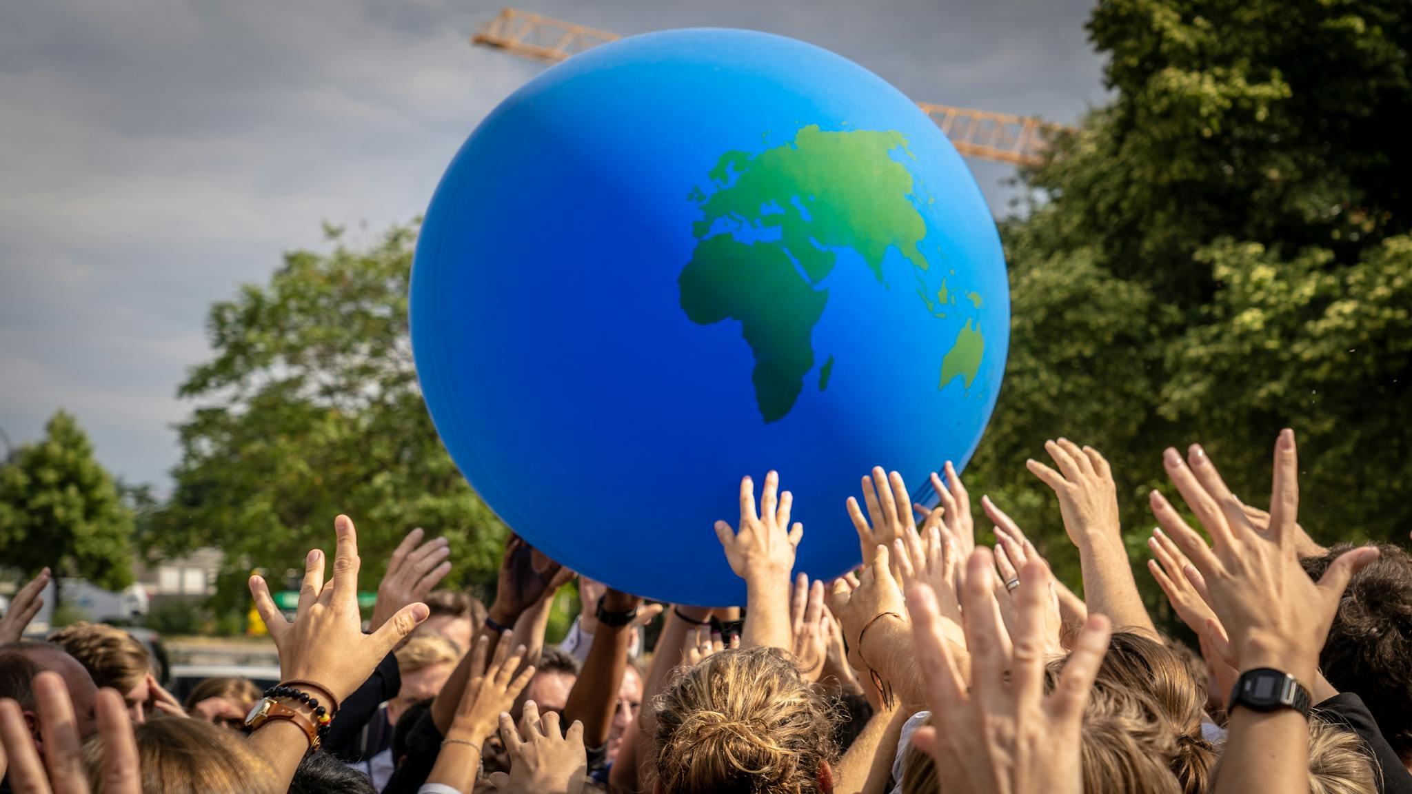 A vibrant scene of people raising hands to a large inflatable globe at a public event in Berlin.